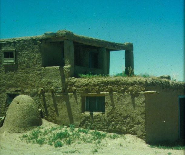 This is an adobe house. It is most common in the Southwestern part of the United States, in the areas formerly occupied by the Spanish. It is built of mud or earthen bricks and features small windows, thick walls and a flat roof. These features make it well suited to the desert environment, where hot days and cool nights are common. The house’s thick walls provide insulation from the heat and radiate heat into the interior during the cool nights. The flat roof is ideal for collecting scarce rainfall. 